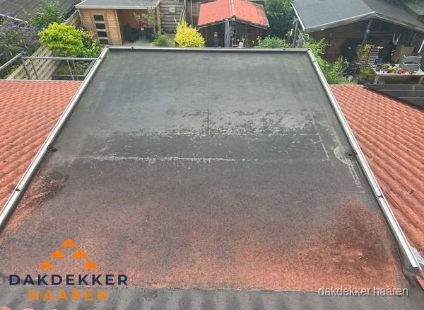 Verouderd plat dak met slijtage tussen schuine daken in Haaren